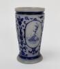 Westerwald stoneware cricket beaker, moulded in relief with three cameo panels of a batsman, after W.G. Grace, in different poses. The body decorated with vine and sprig decoration in cobalt blue on a grey background. Blue rings to rim and to foot. Approx - 2