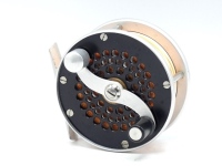 A Bo Mohlin Mini Trout fly reel and block leather case, left hand wind model with black/silver anodised finish, multi-perforated drum and faceplate, serpentine scroll counter-balanced handle, bridge foot, triple cage pillars, fixed check mechanism, backp