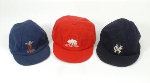 Cricket caps. Three caps, one, a red wool cap with emblem of a bear and &lsquo;Stanford&rsquo; in white thread beneath (Bukta), the next, U.S.CA. navy blue with emblem of a bird (eagle) sitting on a set of stumps with bails, and the third, an older cap, in navy blue,