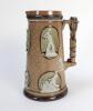 Cricketing jug. A large and impressive Doulton Lambeth stoneware tapering jug, moulded in relief with six raised figures, three of batsman, two of fielders and a wicket keeper in roundels, all different and in various positions. With two further smaller r