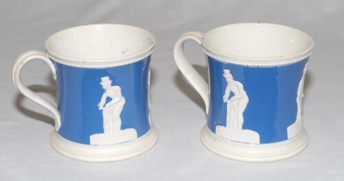 Cricket mugs. A pair of Staffordshire blue ground waisted mugs with strap handle and beaded rim. With three relief moulded figures of a batsman, bowler and wicket keeper in white, believed to be Lillywhite, Pilch and Box. c1860. Rare. Odd marks otherwise 