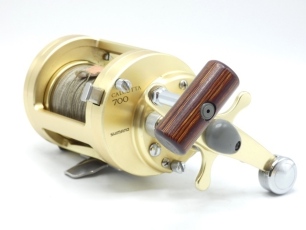 A Shimano Calcutta 700 multiplier reel, gold anodised finish, off-set rosewood T bar handle mounted above a five point capstan star drag, rim drum release button, little used condition, in card box and an un-named 2 piece stand-up carbon boat rod, 8', de