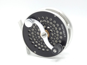 A scarce S.E. Bogdan Trout 5wt fly reel, left hand wind model with silver/black anodised finish, counter-balanced serpentine crank handle, pierced foot, fixed click check mechanism, multi-perforated drum and faceplate, rear milled spindle cap and applied 