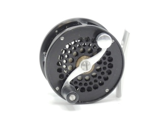 A scarce S.E. Bogdan Small trout 3wt fly reel, black anodised finish, left hand wind model with serpentine counter-balanced crank winding arm set within an anti-foul rim, multi-perforated front drum and faceplate, pierced alloy block foot, fixed click che