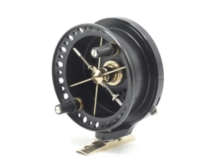 A J.W. Young Ray Walton Rolling Pin Mk.II 3 ¾" wide drummed turntable reel, black anodised finish, six spoked shallow cored drum with twin composition handles and release/regulator forks, spring locking swivelling stancheon foot and rim mounted optional c