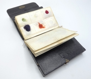 A scarce W.J. Cummins black rexine rectangular fly tyer's wallet, interior fitted lidded four section compartment for bobbins, hooks etc. with brass hasp latch, twelve parchment material leaves holding various dubbings, wools et al, end pouch pocket and