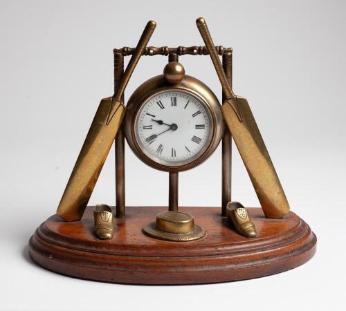 Cricket clock. A Victorian brass mantel clock. An attractive late Victorian/ Edwardian brass clock of cricketing interest, formed with a central drum form enamelled dial, encased within a set of cricket stumps and bails with cricket bats leaning against t