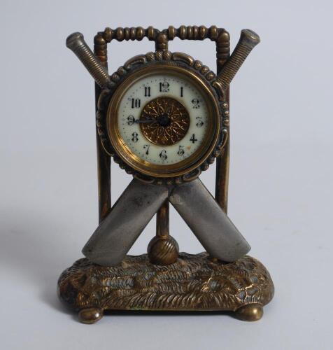 Cricket clock. A Victorian brass mantel clock. The case in the form of a set of stumps with crossed bats and ball on an oval naturalistic case base with bun feet. Dial with gilded centre. Approximately 6.5” high by 5” wide. British Union Clock Company sta