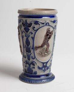 Westerwald stoneware cricket beaker, moulded in relief with three cameo panels of a batsman, after W.G. Grace, in different poses. The body highly decorated with vine and sprig decoration in cobalt blue on a grey background, with the figures highlighted i