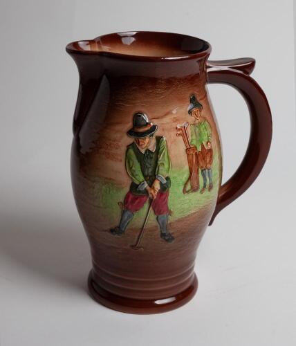 A large Royal Doulton ‘Airbrush Brown’ Kingsware lemonade jug with a golf scene of cavalier golfer with caddie (Charles Crombie) to one side and a smaller group playing golf to verso. Royal Doulton mark and No. 5716 is on the bottom of the jug. 9.5” tall.