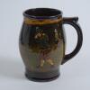 Royal Doulton Kingsware brown mug/tankard with a golf scene of cavalier golfer with caddie (Charles Crombie) to one side and a smaller group playing golf to verso. Royal Doulton mark to the bottom of the mug. 5.5” tall. Circa 1930. Very good condition