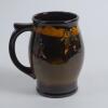 Royal Doulton Kingsware brown mug/tankard with a golf scene of cavalier golfer with caddie (Charles Crombie) to one side and a smaller group playing golf to verso. Royal Doulton mark to the bottom of the mug. 5.5” tall. Circa 1930. Very good condition - 2