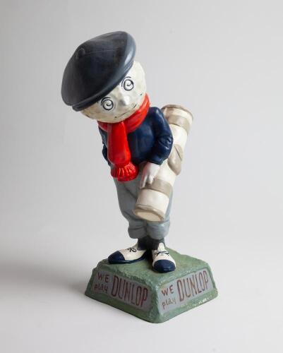 A large and colourful advertising golf figure in the form of a caddie with a golf ball head. The base has the slogan in relief: “We play DUNLOP”. These figures would have been displayed on the counters in the sports shops to advertise Dunlop golf balls. A