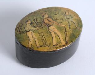 Cricket snuff box. An oval black lacquered papier mache snuff box with hinged lid, believed to be circa 1870&rsquo;s. The lid painted with a cricketing scene of boys playing cricket with trees in background. The box measures approx 2.75&rdquo; x 2&rdquo;x 1.25&rdquo; deep. Good 