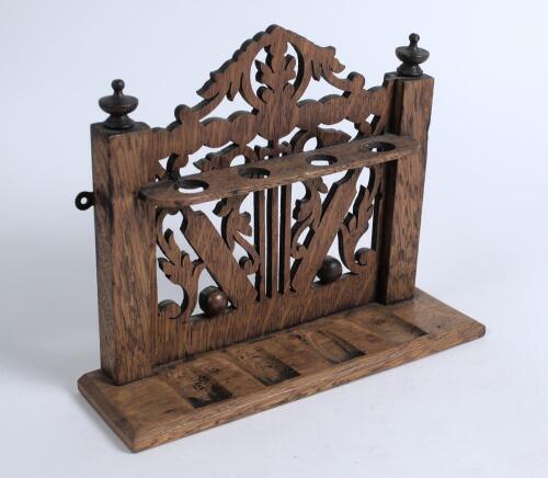 Wooden pipe rack. Nice pipe rack with slots for four pipes and intricate fret work, the design featuring two cricket bats and balls with turned finials. Hand written date &lsquo;1914&rsquo; to base. Small loss to one finial, otherwise in good condition