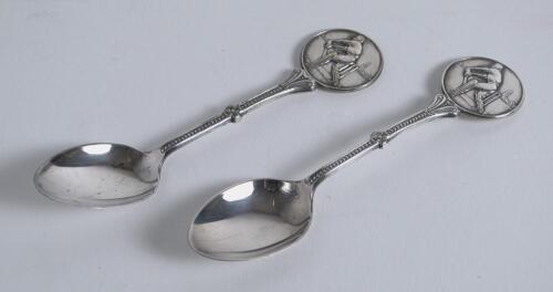 Cricket spoons. A pair of silver plated spoons each with a similar figure of a batsman at the wicket to top of handle. Sold with a small ceramic cricket cup with image of a batsman and a golfing saucer, cracks to the saucer. G