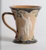 Doulton Lambeth stoneware mug in art nouveau style, with three moulded relief vignettes of cricketers, a batsman, bowler and wicket keeper, Abel, Woods and McGregor in white on a brown background, with floral leaf decoration above and below in green and g