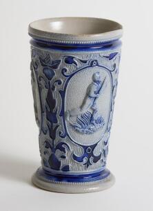 Westerwald stoneware cricket beaker, moulded in relief with three cameo panels of a batsman, after W.G. Grace, in different poses. The body highly decorated with vine and sprig decoration in cobalt blue on a grey background, with the figures highlighted i