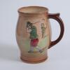 Royal Doulton &lsquo;Airbrush Brown&rsquo; Kingsware mug/tankard with a golf scene of cavalier golfer with caddie (Charles Crombie) to one side and a smaller group playing golf to verso. Royal Doulton mark and No. 5716 to the bottom of the mug. 5.5&rdquo; tall. Circa 1930
