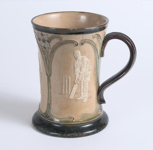 Doulton Lambeth stoneware waisted ceramic tankard with three moulded relief vignettes of cricketers, a batsman, bowler and wicket keeper in white on brown background. With stylised floral leaf and flower decoration to top and beneath in green, brown and l