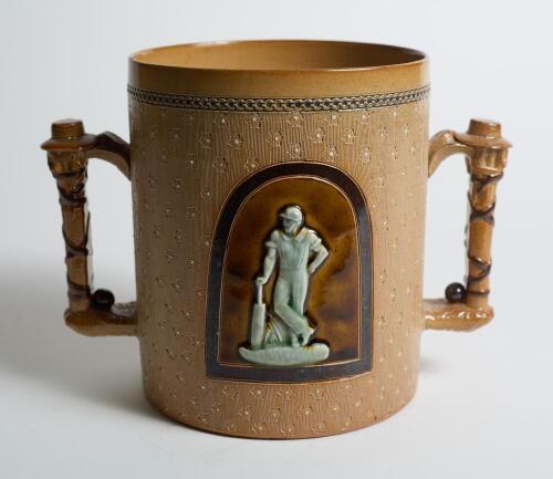 Doulton Lambeth large stoneware two handled loving cup, in brown, impressed with a delicate white flower and floral decoration, with two moulded relief vignettes in roundels of a batsman stood leaning on his bat and a wicket-keeper breaking the stumps wit