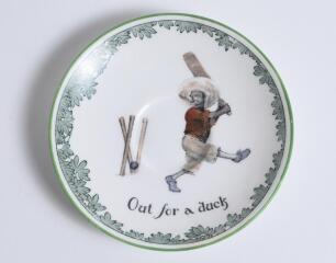 &lsquo;Out for a Duck&rsquo; Royal Doulton Black Boy saucer, entitled &lsquo;Out for a Duck&rsquo; printed with a boy in red shirt and a floppy hat in batting pose having attempted a big shot, looking back to see the ball hit his wicket. Green floral decoration to edge. 5.5&rdquo; dia