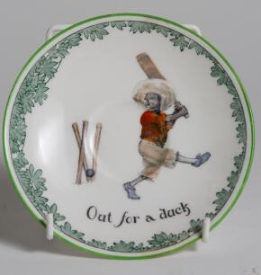 &lsquo;Out for a Duck&rsquo;. A Royal Doulton Black Boy plate, entitled &lsquo;Out for a Duck&rsquo; printed with a boy in red shirt and a floppy hat swinging the bat and being bowled out, the wicket broken. Green floral decoration to outer rim. 9.5&rdquo; diameter. Doulton backstamp 