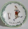 &lsquo;Out for a Duck&rsquo;. A Royal Doulton Black Boy plate, entitled &lsquo;Out for a Duck&rsquo; printed with a boy in red shirt and a floppy hat swinging the bat and being bowled out, the wicket broken. Green floral decoration to outer rim. 9.5&rdquo; diameter. Doulton backstamp 