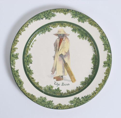 &lsquo;The Boss&rsquo; Royal Doulton Black Boy dinner plate, entitled &lsquo;The Boss&rsquo; printed with a boy in red shirt and a floppy hat, wearing an umpires&rsquo;s coat and holding a bat. Green floral decoration to outer rim. 9.5&rdquo; diameter. Doulton backstamp and number &lsquo;D2864&rsquo; t