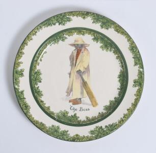 &lsquo;The Boss&rsquo; Royal Doulton Black Boy dinner plate, entitled &lsquo;The Boss&rsquo; printed with a boy in red shirt and a floppy hat, wearing an umpires&rsquo;s coat and holding a bat. Green floral decoration to outer rim. 9.5&rdquo; diameter. Doulton backstamp and number &lsquo;D2864&rsquo; t