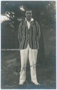 Kumar Shri Duleepsinhji. Sussex, Cambridge University & England 1924-1932. Excellent original mono real photograph postcard of Duleep standing full length under a tree, wearing cricket attire and striped blazer. The postcard very nicely signed in black in