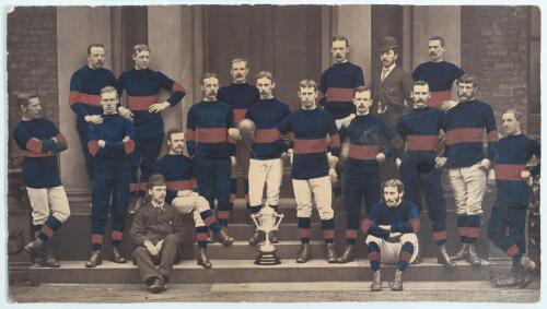 Rugby Union. Wakefield Trinity Rugby Football Club c.1879. Large and early original mono photograph heightened in club colours of red and blue of the Wakefield Trinity team with the Yorkshire Challenge Cup trophy, standing on the stone steps of what appea
