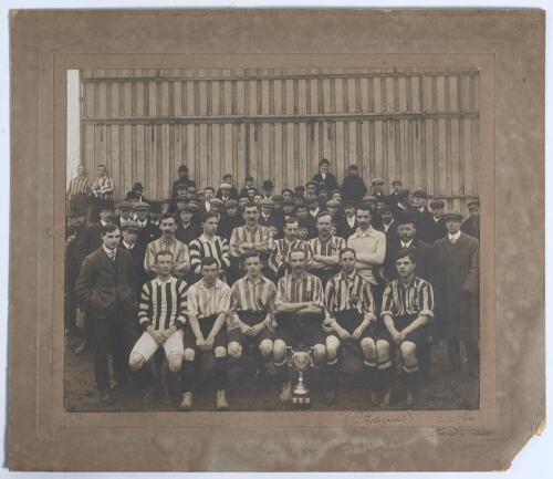 Ipswich Town F.C. 1906/07. Early original sepia photograph of the Ipswich Town team seated and standing in rows wearing football attire with officials and the crowd behind, and a trophy in front (probably a local Suffolk tournament). Players featured appe