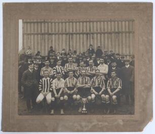 Ipswich Town F.C. 1906/07. Early original sepia photograph of the Ipswich Town team seated and standing in rows wearing football attire with officials and the crowd behind, and a trophy in front (probably a local Suffolk tournament). Players featured appe