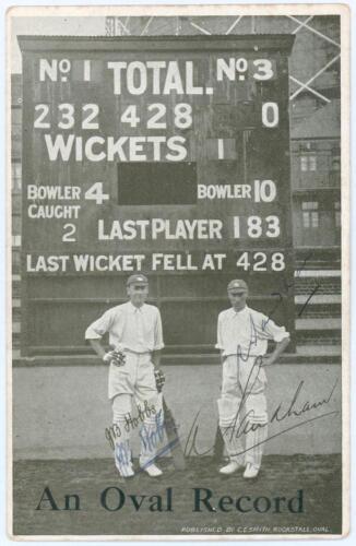 Jack Hobbs and Andrew Sandham. Surrey. Mono postcard of Hobbs and Sandham, the pair standing in front of The Oval scoreboard, titled &lsquo;An Oval Record&rsquo; with printed signatures and additionally signed in ink by both players. The scoreboard shows the opening 
