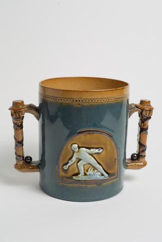 Doulton Lambeth large stoneware two handled loving cup, in brown overlaid unusually with blue glaze, impressed with a beaded decoration to rim, with two moulded relief vignettes in roundels of a wicket-keeper breaking the stumps with the ball and a fielde
