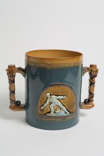 Doulton Lambeth large stoneware two handled loving cup, in brown overlaid unusually with blue glaze, impressed with a beaded decoration to rim, with two moulded relief vignettes in roundels of a wicket-keeper breaking the stumps with the ball and a fielde