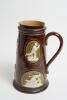 Cricketing jug. A large and impressive Doulton Lambeth stoneware tapering jug in a dark brown mottled colour, moulded in relief with six raised figures, three of batsman, two of fielders and a wicket keeper in roundels, all different and in various positi