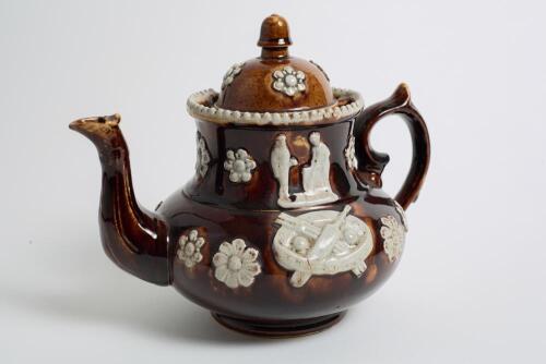 Measham Ware cricket teapot. A Victorian saltglaze stoneware brown teapot with lid. The teapot with sprigged decoration in white of two cricket figures, believed to be Pilch and Box to each side, below the figures are sprigged crossed bat and stumps with 