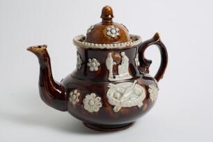 Measham Ware cricket teapot. A Victorian saltglaze stoneware brown teapot with lid. The teapot with sprigged decoration in white of two cricket figures, believed to be Pilch and Box to each side, below the figures are sprigged crossed bat and stumps with 