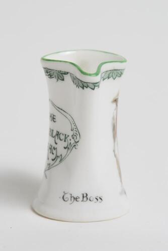 &lsquo;The Boss&rsquo;. Royal Doulton Black Boy miniature flared lip jug, with printed image of a boy in red shirt and a floppy hat, wearing an umpire&rsquo;s coat with bat to side, title to side. To verso a crest with &lsquo;The All Black Team&rsquo;. Green floral decoration to outer