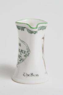 &lsquo;The Boss&rsquo;. Royal Doulton Black Boy miniature flared lip jug, with printed image of a boy in red shirt and a floppy hat, wearing an umpire&rsquo;s coat with bat to side, title to side. To verso a crest with &lsquo;The All Black Team&rsquo;. Green floral decoration to outer