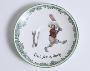 &lsquo;Out for a Duck&rsquo; Royal Doulton Black Boy saucer, entitled &lsquo;Out for a Duck&rsquo; printed with a boy in red shirt and a floppy hat in batting pose having attempted a big shot, looking back to see the ball hit his wicket. Green floral decoration to edge. 5.5&rdquo; dia