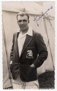 Leslie Ethelbert George &lsquo;Les&rsquo; Ames. Kent & England 1926-1951. Mono real photograph postcard of Ames standing three quarter length behind a marquee, wearing an M.C.C. blazer for the 1932/33 &lsquo;Bodyline&rsquo; tour to Australia. Nicely signed in blue ink to the pho