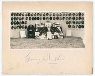 William Ambrose &lsquo;Billy&rsquo; Wright. Wolverhampton Wanderers & England 1939-1959. Original mono photograph of Wright c.1960 seated beside a table with trophies, jerseys, pennants etc. from his playing career. Hanging on the wall behind are seventy one England 