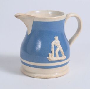 Cricket jug. Small early Staffordshire blue cream/milk cricket jug with strap handle, Blue background and two raised figures of a batsman playing back to either side. c1870/80. 3&rdquo; tall. Minor firing crack to handle otherwise in good/very good condition. A