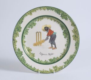 &lsquo;There&rsquo;s Style!&rsquo;. A Royal Doulton Black Boy dinner plate, entitled &lsquo;There&rsquo;s Style!&rsquo; printed with a boy in red jacket and a floppy hat stood in batting stance in front of the wicket. Green floral decoration to inner and outer rim. 9.5&rdquo; diameter. Doulton ba