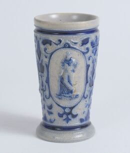 Westerwald stoneware cricket beaker, moulded in relief with three cameo panels of a batsman, after W.G. Grace, in different poses. The body highly decorated with vine and sprig decoration in cobalt blue on a grey background, with the figures highlighted i