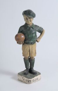 &lsquo;The Captain&rsquo;. Early plaster figure of a boy in football attire holding a brown football to side with hand on his hip. The boy is wearing a green jersey, yellow shorts, green socks and green cap. &lsquo;Captain&rsquo; inscribed to the chest of the boy&rsquo;s jersey. To ba