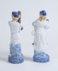 Cricket figures. A pair of German porcelain figures, the boy holding a cricket bat, wearing pads with a cap, the girl in three quarter length dress wearing a cap, she is holding a ball. Each figure is beautifully decorated in blue, red and gold lustre. 9&rdquo; - 2